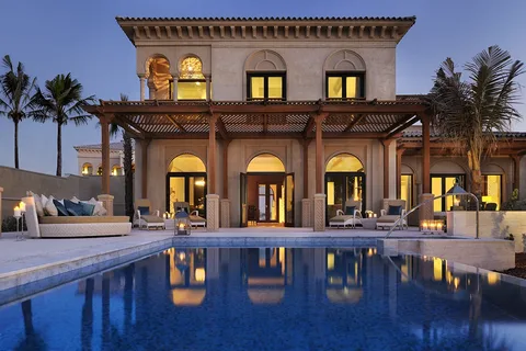 The image features a house with a pool and a large pool. It includes elements such as trees, sky, water, and palm trees. Overall, it conveys a sense of a luxurious outdoor setting with a focus on a property with a pool.